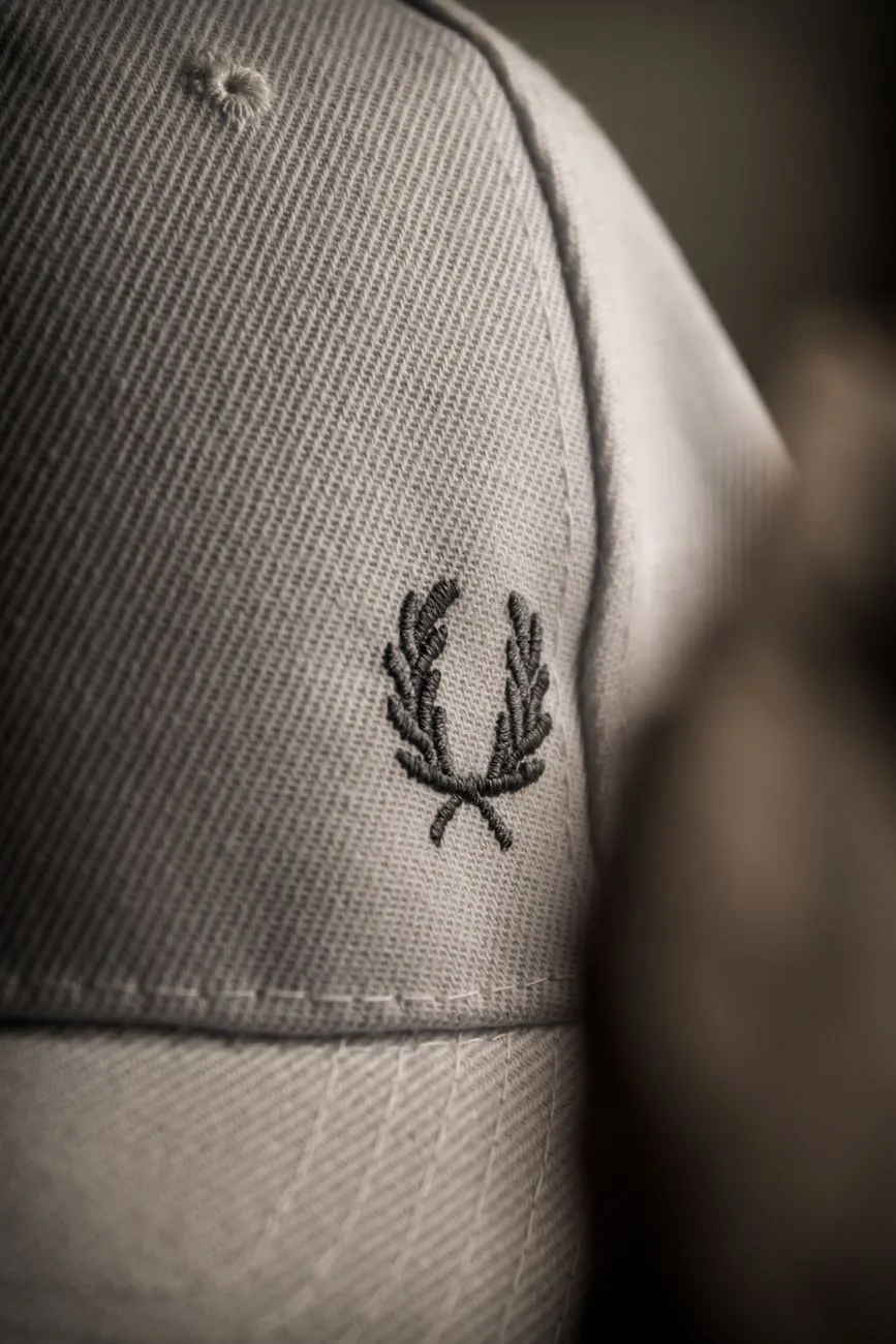 Gros plan d’une casquette beige brodée de branches d’olivier, avec la texture du tissu et la courbure visible