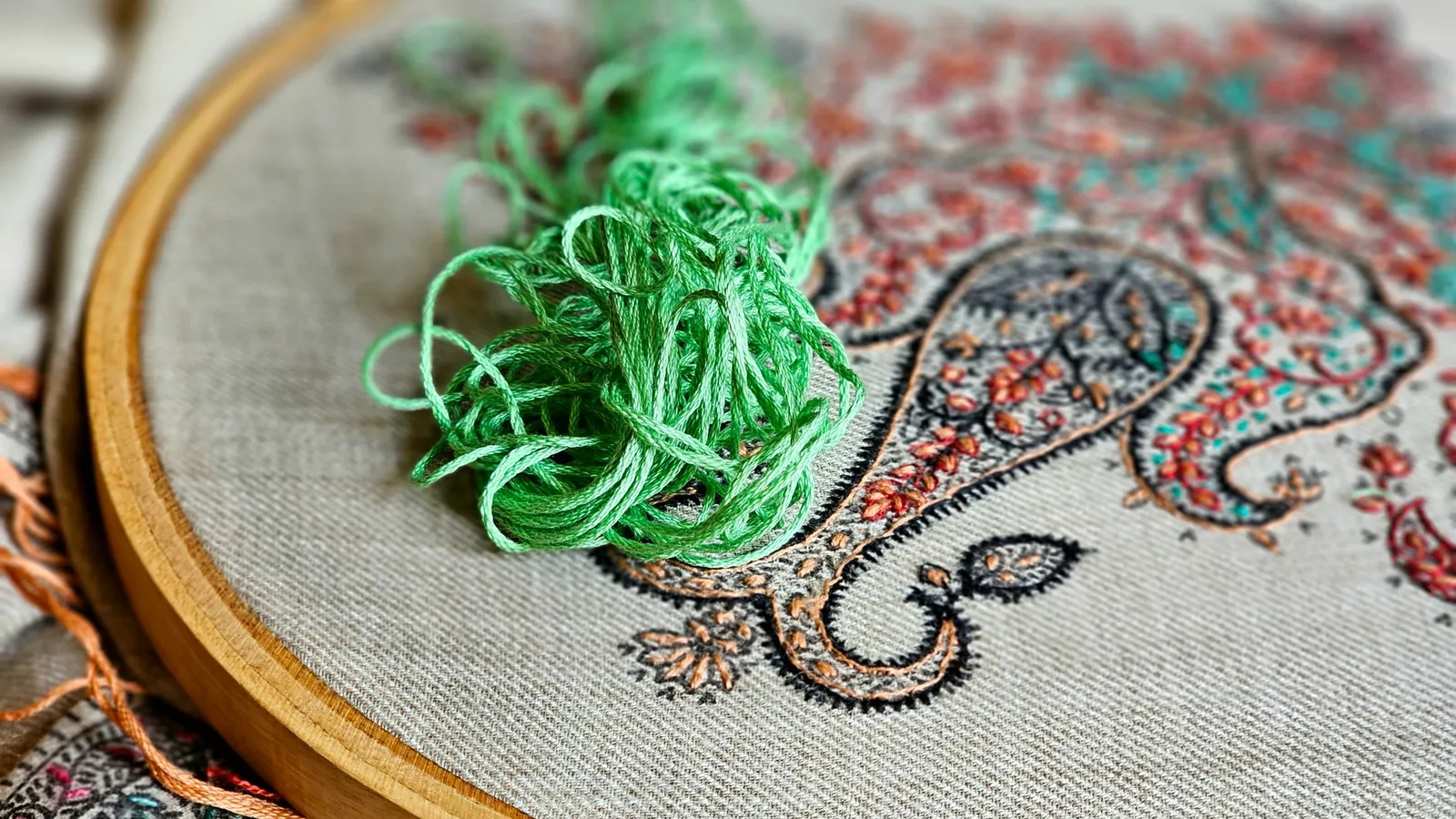 Gros plan d'une broderie au fil vert sur un tissu à motif cachemire, avec le relief des points visible