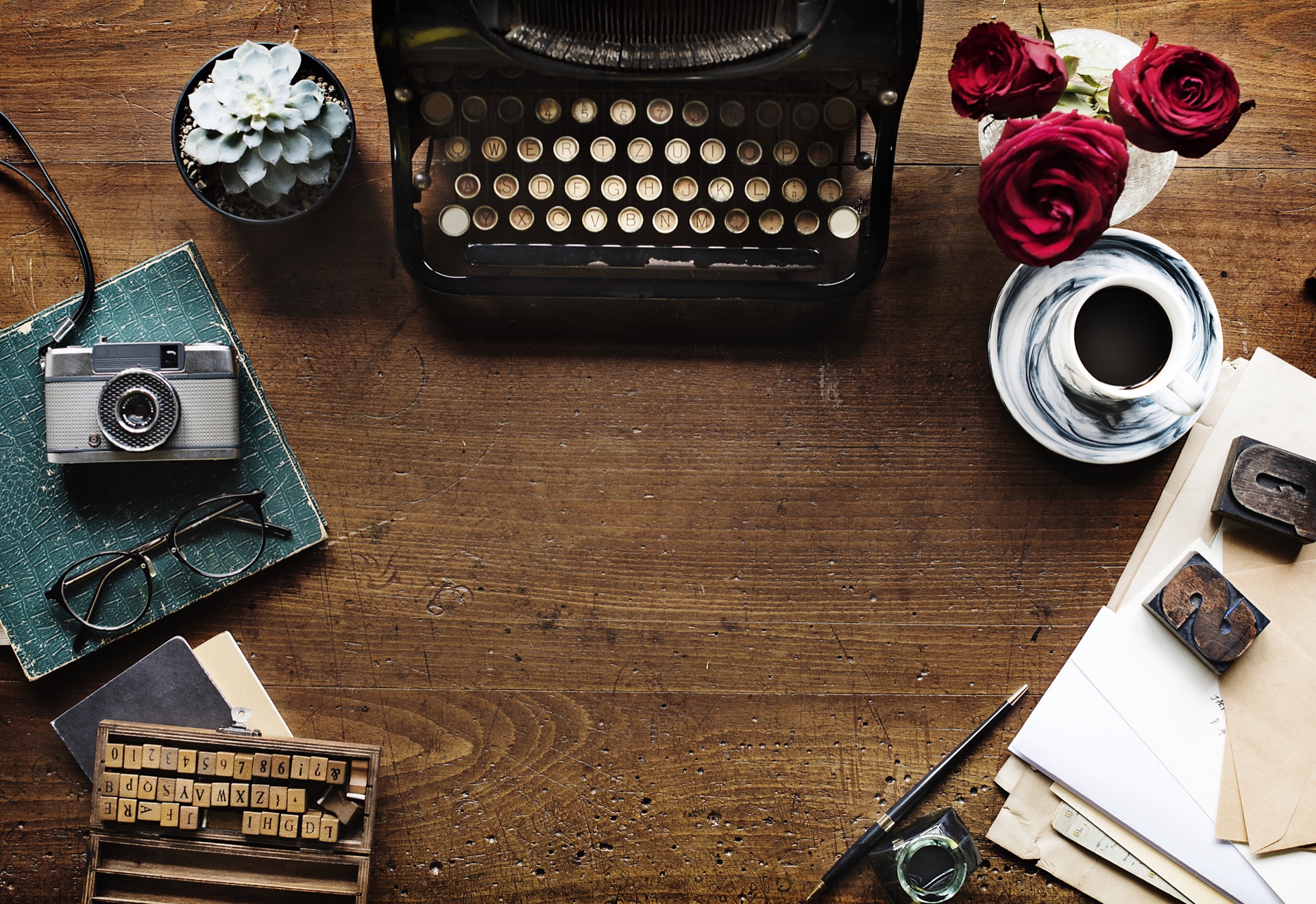 Vue de dessus d'un bureau en bois avec machine à écrire ancienne, tampons alphabet, caractères en bois, papiers et tasse de café