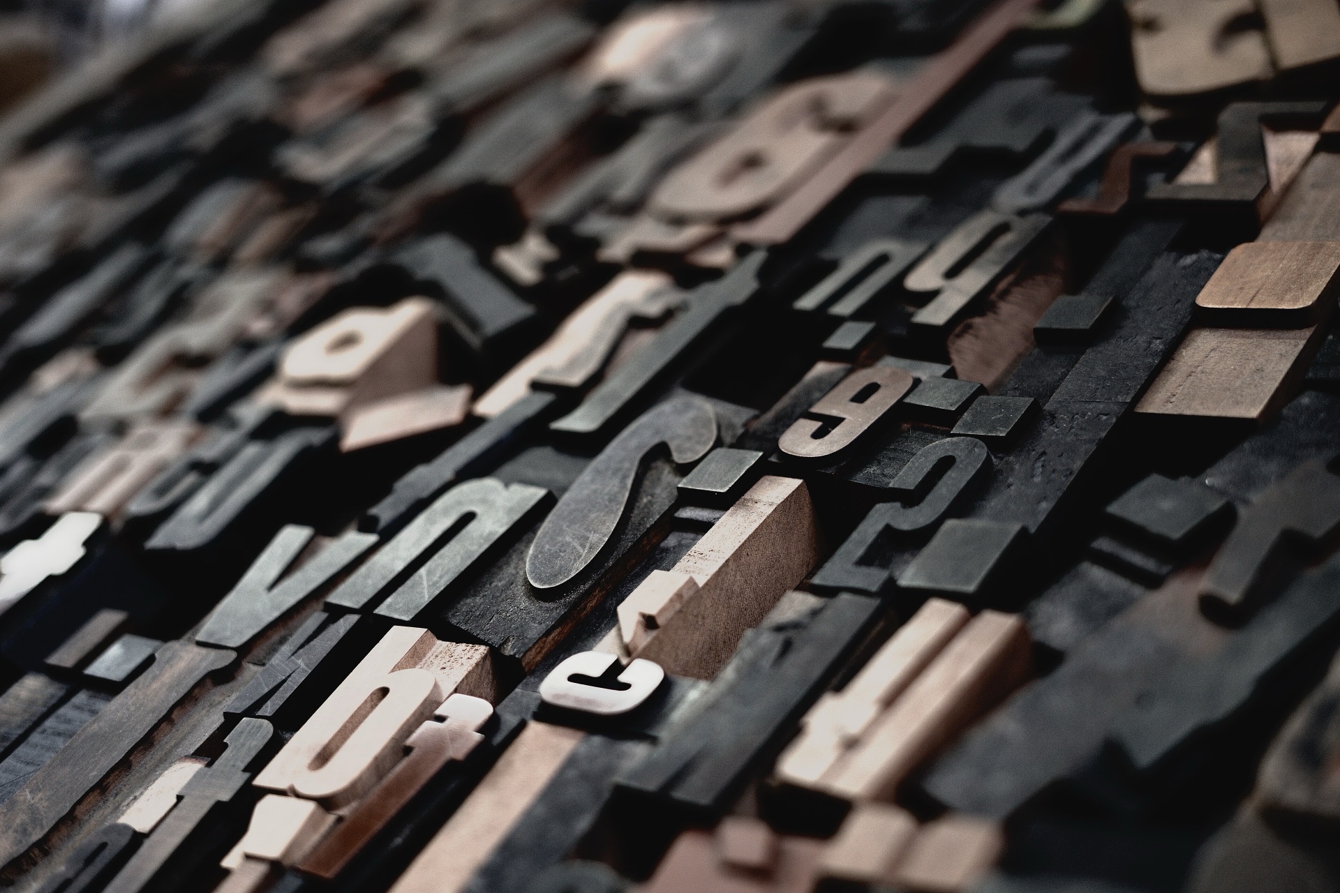 Gros plan sur des caractères typographiques en bois patinés, alignés dans la pénombre d'un atelier
