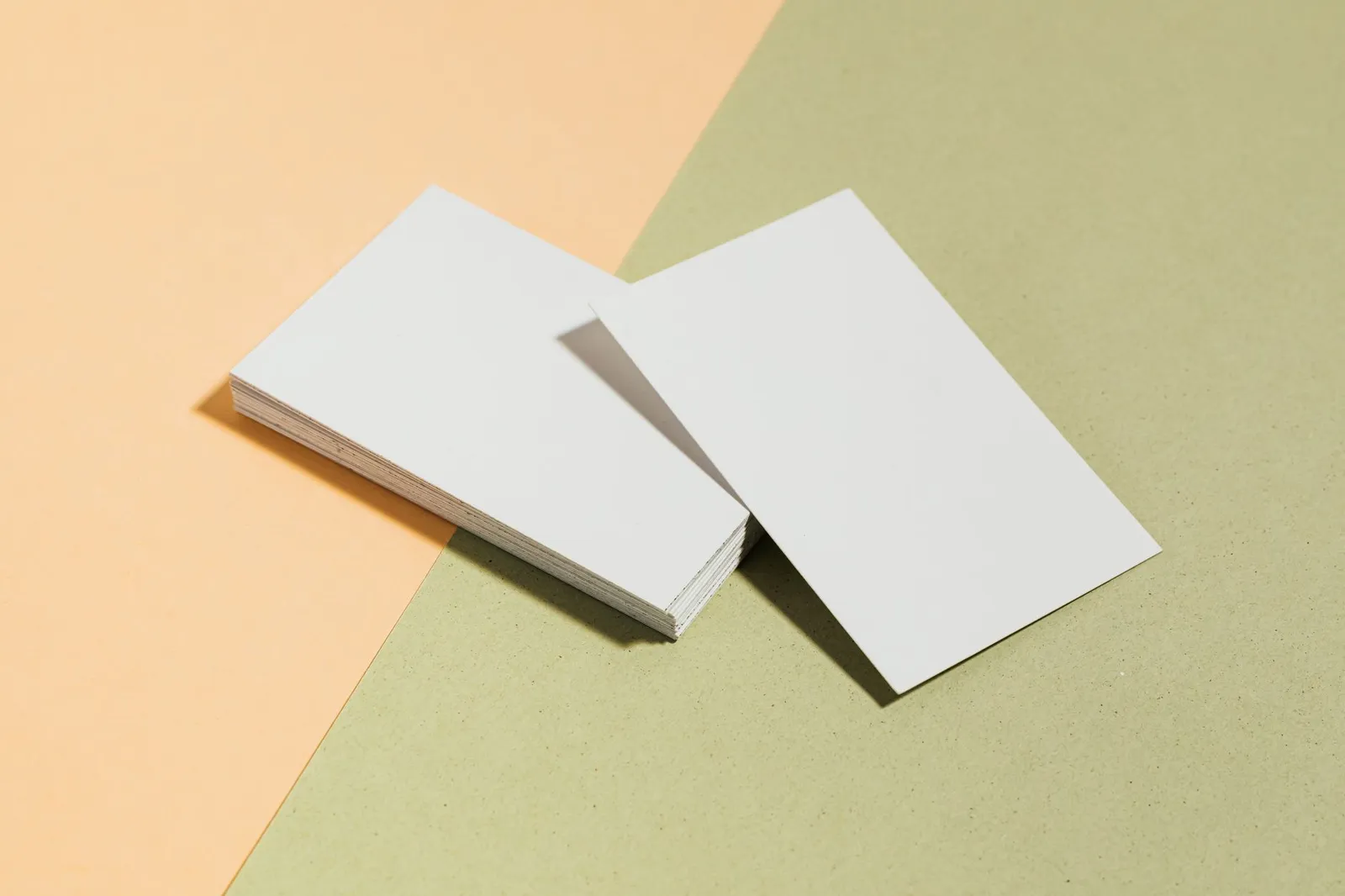 Deux piles de cartes de visite blanches vierges, l’une plus épaisse que l’autre, sur un fond pastel
