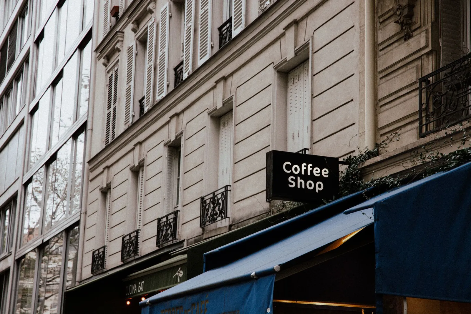 Façade de café en rue, avec bandeau sobre et petite enseigne, devanture colorée sans marque lisible