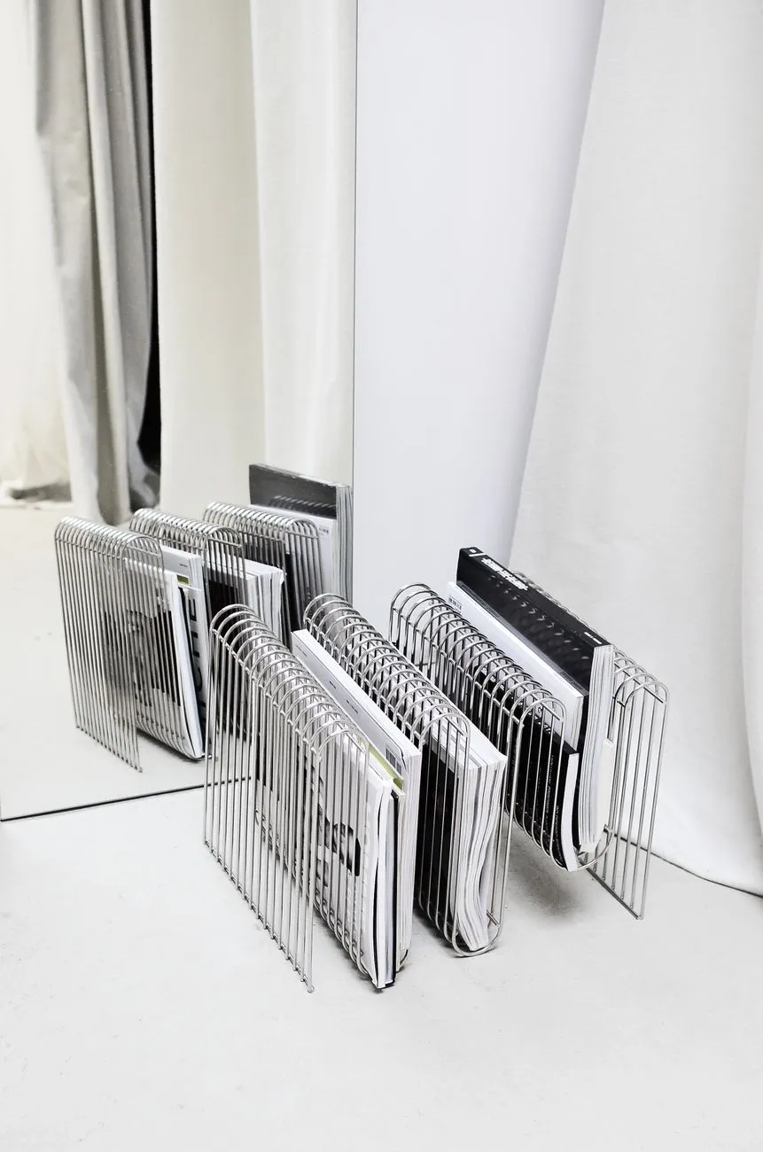 Porte-revues en métal avec plusieurs brochures et magazines alignés dans un intérieur minimaliste