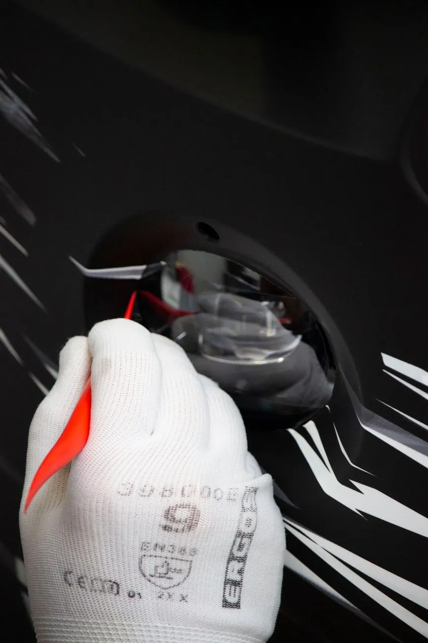 Mains gantées posant un autocollant de course sur une carrosserie noire, avec un bord encore soulevé