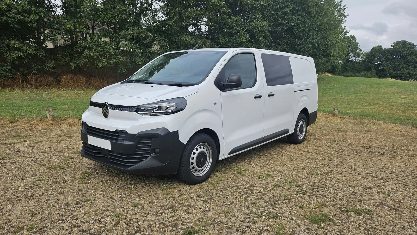 Fourgon utilitaire blanc stationné sur du gravier en extérieur, vu de trois quarts avant, sans marque visible