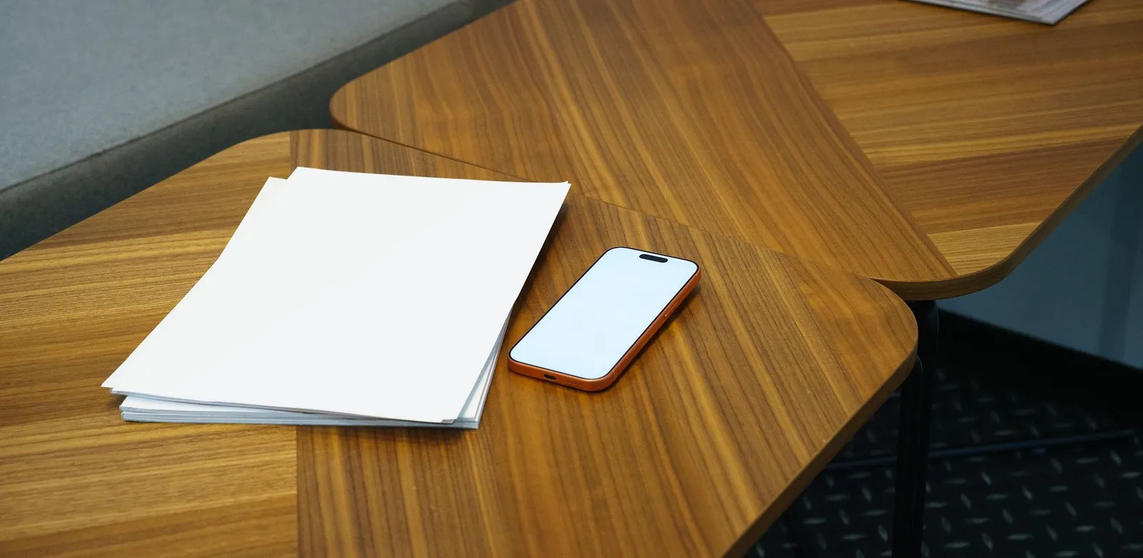 Pile de flyers blancs posée sur un bureau en bois, à côté d’un smartphone, sans texte lisible ni marque visible