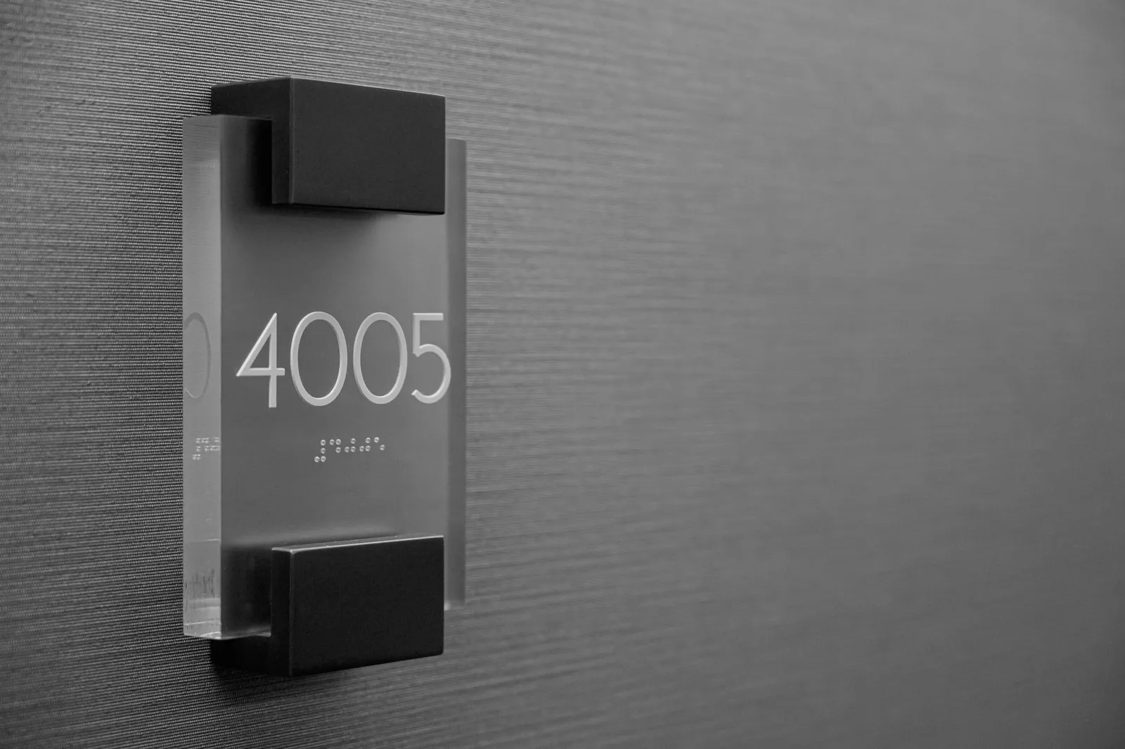 Plaque de porte minimaliste avec le numéro 4005 en relief et des points en braille en dessous, sur fond gris
