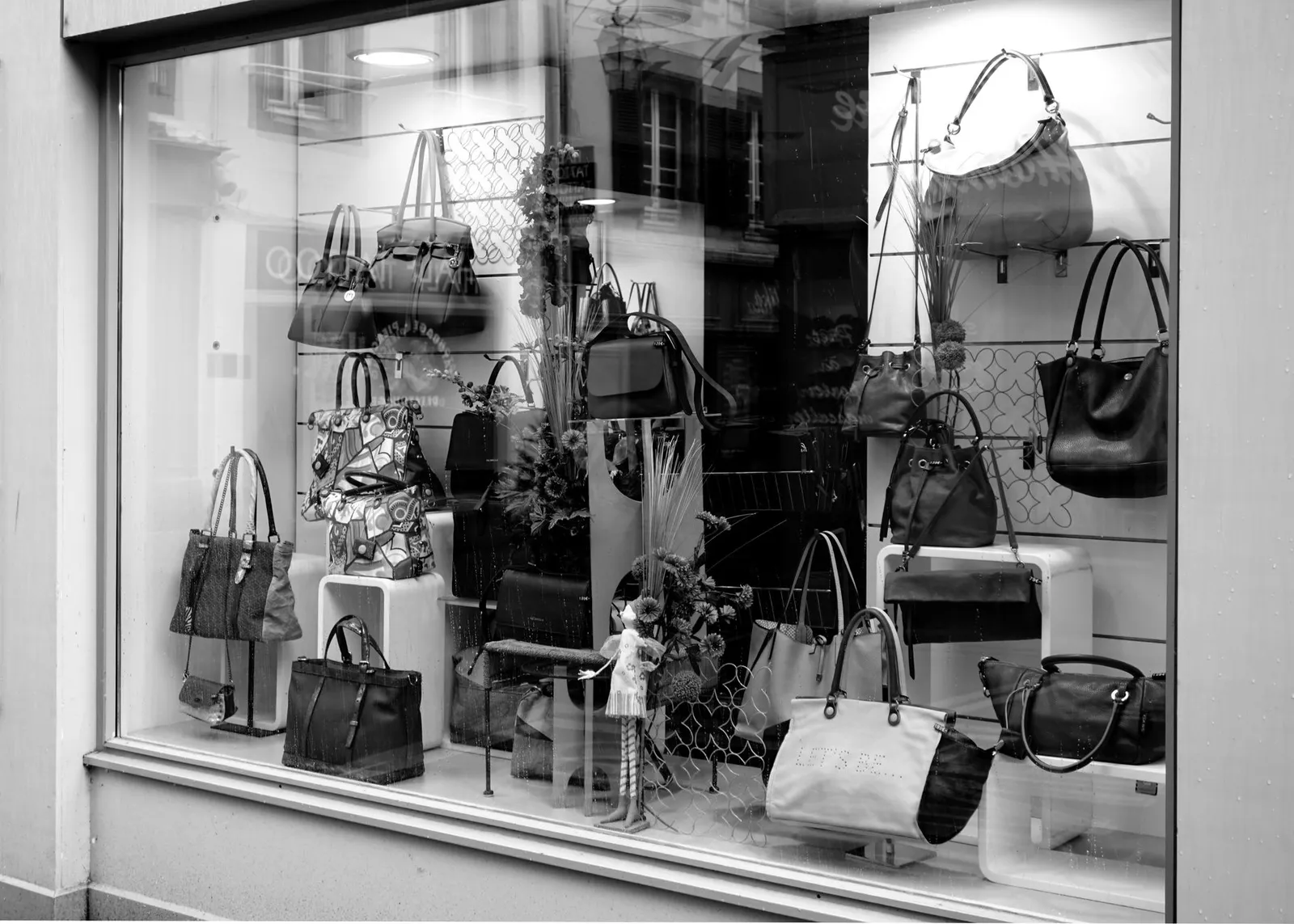 Vitrine de boutique vue de l’extérieur, avec sacs exposés derrière la vitre et reflets sur le verre